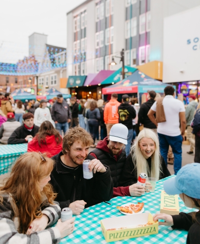 People enjoying food and drinks at picnic tables during a street feast in Charlottetown, Prince Edward Island