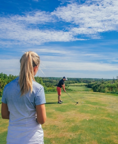 A scenic golf course in Prince Edward Island with lush green fairways, trees, and ocean views on a sunny summer day.
