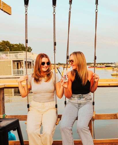Guests relaxing on swing seats at JC Tiki Bar's waterfront patio overlooking Charlottetown Harbour in Prince Edward Island.