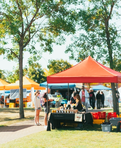 Outdoor vendors and shoppers at the Charlottetown Farmers’ Market, browsing fresh produce, baked goods, and handmade products on a sunny summer day.