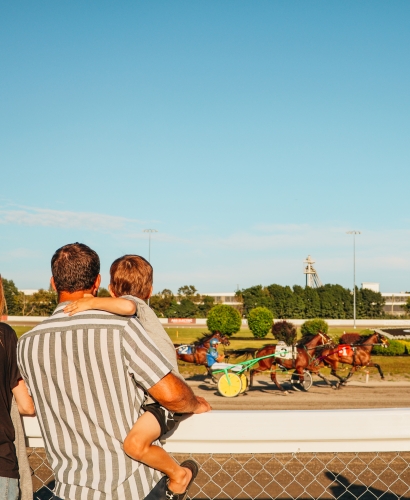 Crowds watching harness horse racing during Race Week at Red Shores Racetrack & Casino in Charlottetown, PEI, with horses racing around the track.