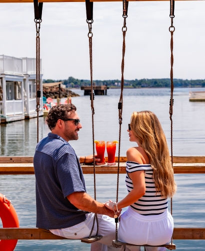Guests relaxing on waterfront swings at JC Tiki Bar overlooking Charlottetown Harbour in Prince Edward Island.